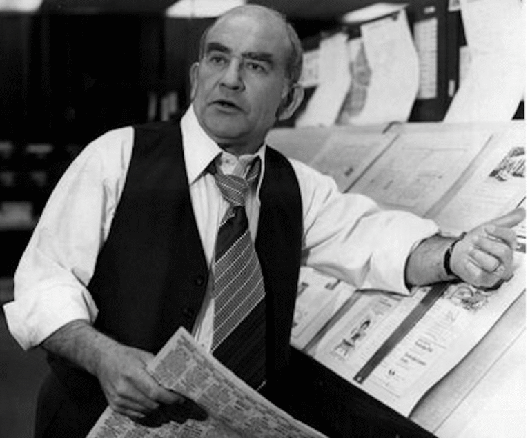 Ed Asner in a scene reminiscent of his role as a newspaper editor, holding a newspaper.