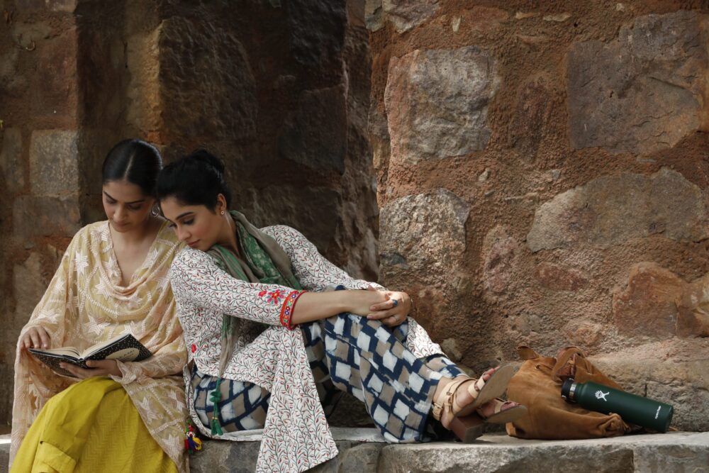 Two women reading near a stone wall.