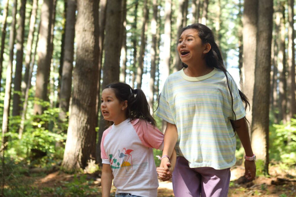 Two young girls holding hands in a forest.