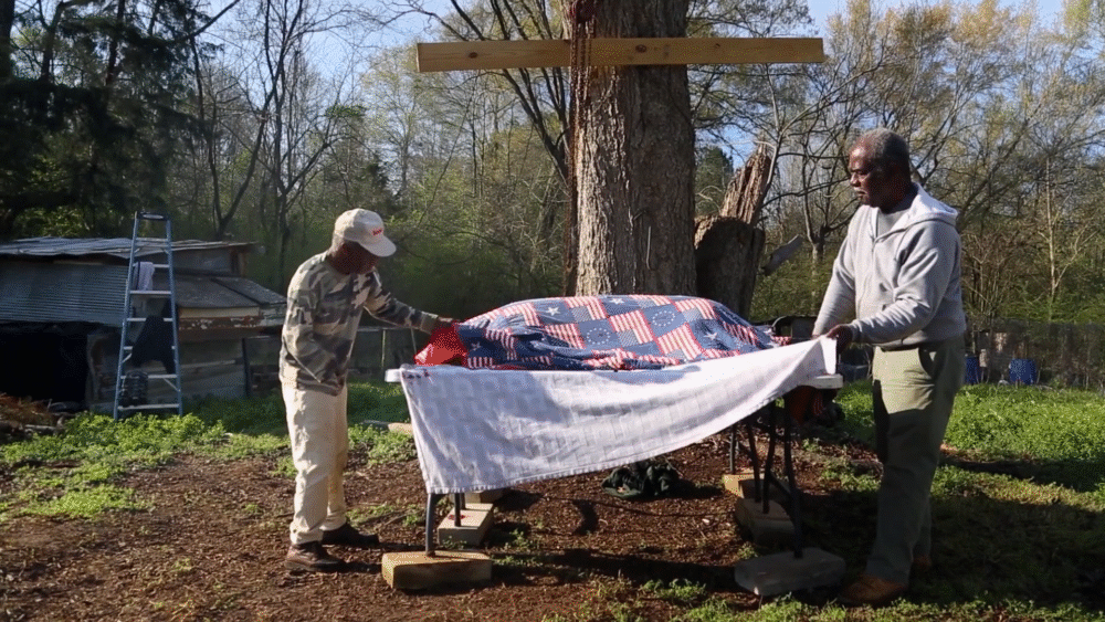 Two men prepare a flag-draped object outdoors.