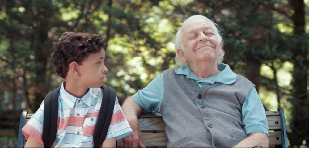 Boy and elderly man sitting on a park bench, enjoying the sun.