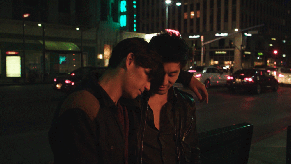Two men embracing in city at night, showing queer love.