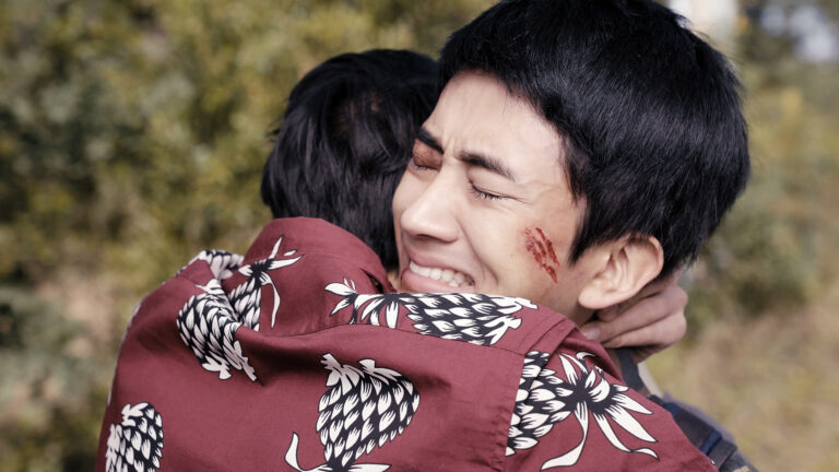 Emotional embrace between two men, one with a facial scratch, capturing a dramatic moment.