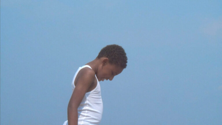 Black boy in white tank top looking down against a clear blue sky. "What If Black Boys Were Butterflies?