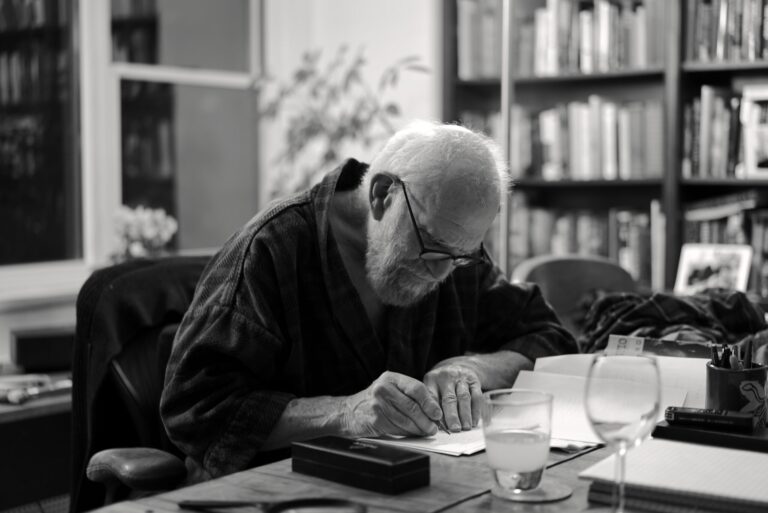 Oliver Sacks writing at his desk, surrounded by books.