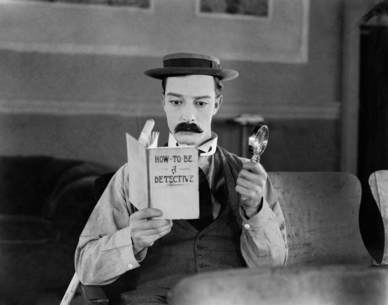 Buster Keaton reading "How-To-Be a Detective" with a magnifying glass.