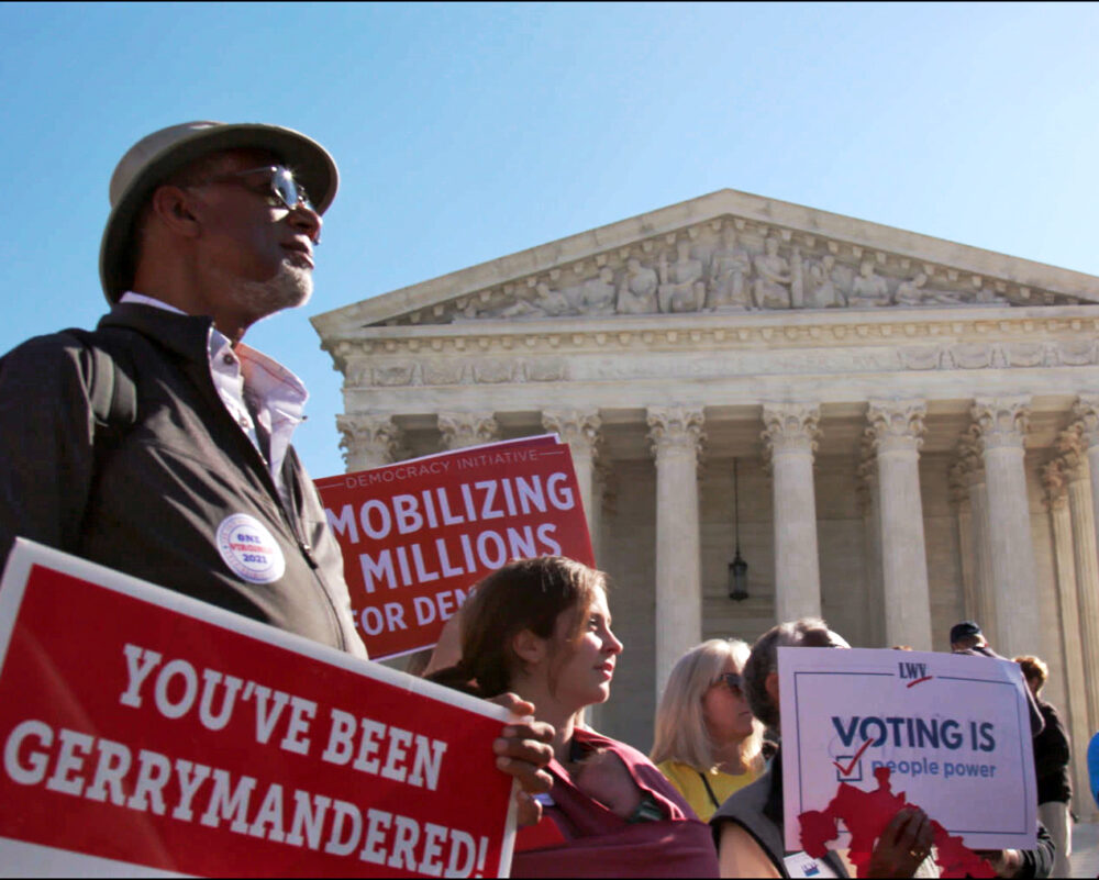 People protesting gerrymandering in front of the Supreme Court, holding signs.