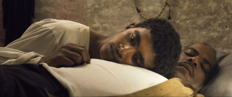 Still from "You Will Die at 20": A young man rests on an older man's chest.