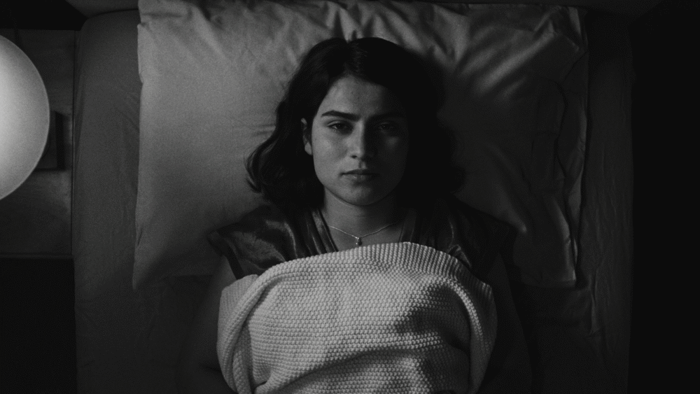 Black and white image of a woman lying in bed, wrapped in a blanket.
