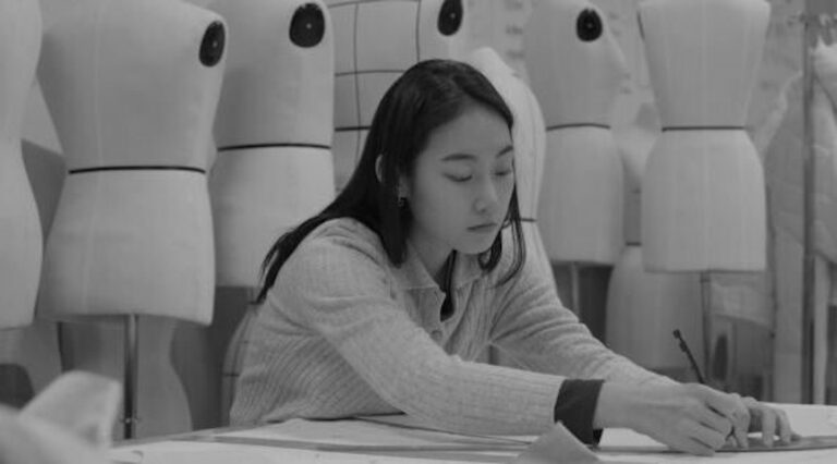 Fashion designer sketching at a desk surrounded by dress forms.