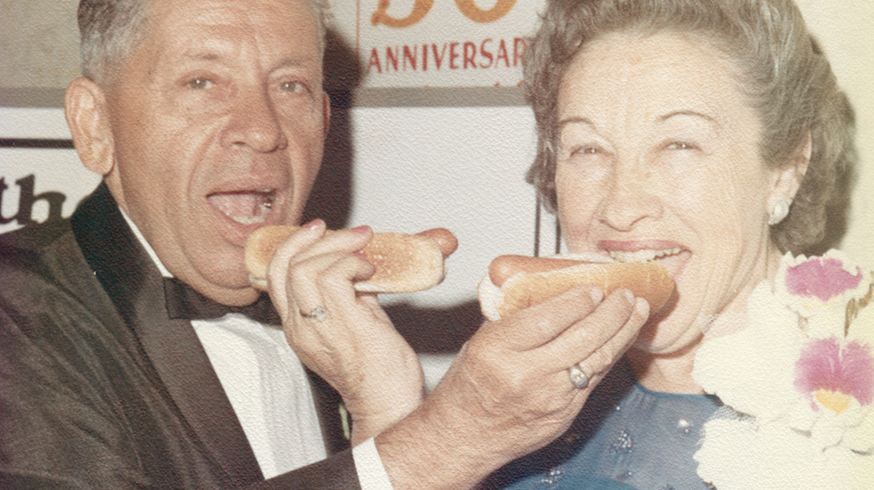 Nathan's Famous founders eating hot dogs at anniversary. "50th Anniversary" text visible.
