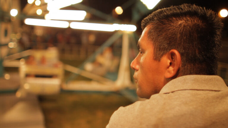 Man looks at a blurred Ferris wheel at night, hinting at "Farewell Ferris Wheel"