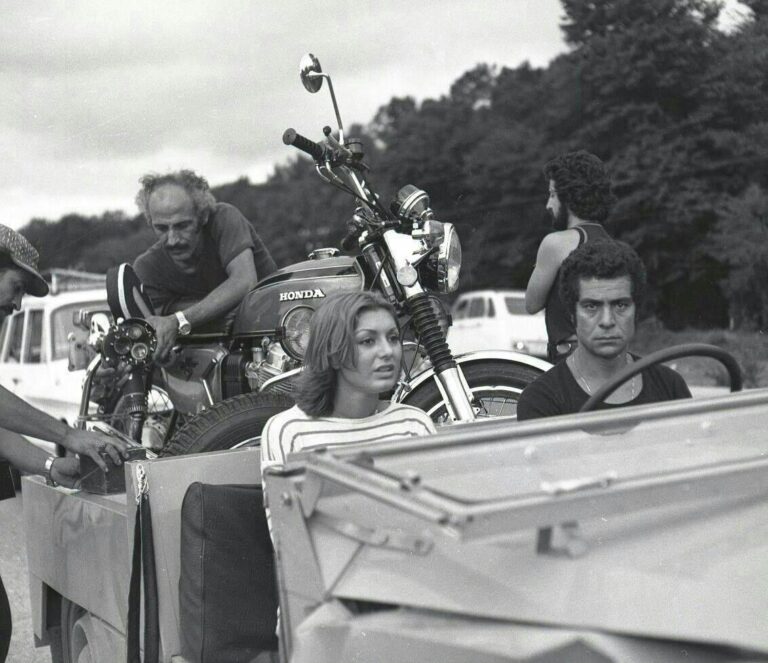 People with a vintage Honda motorcycle and a vehicle, possibly related to Filmfarsi.