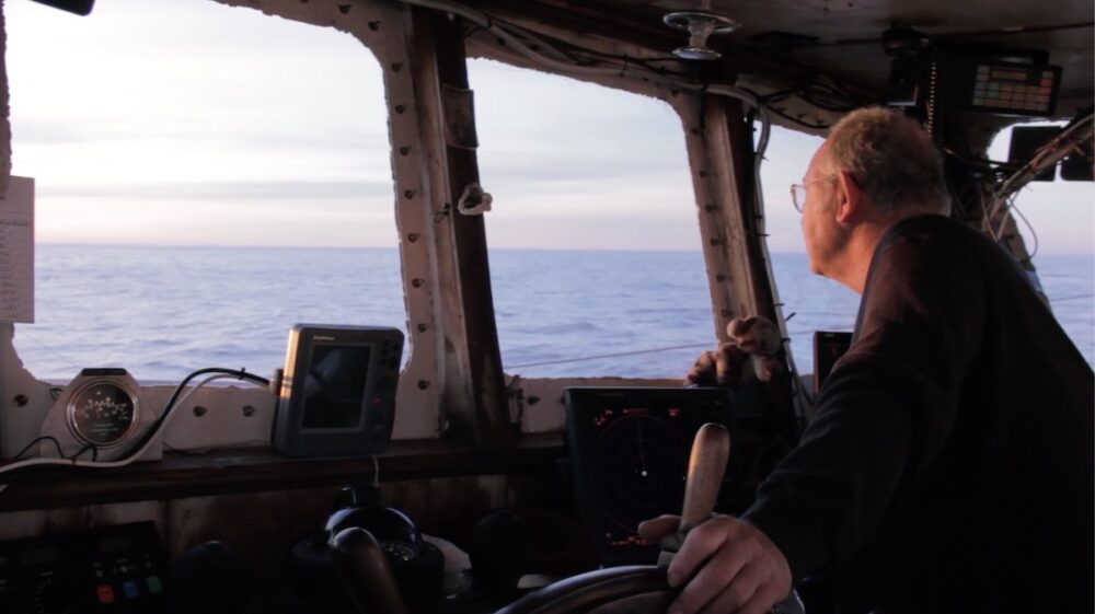 Fisherman at the helm of a boat, looking out at the ocean.