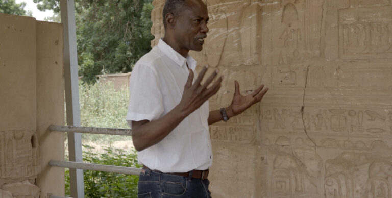 Sudanese man gesturing near ancient carvings in Sudan.