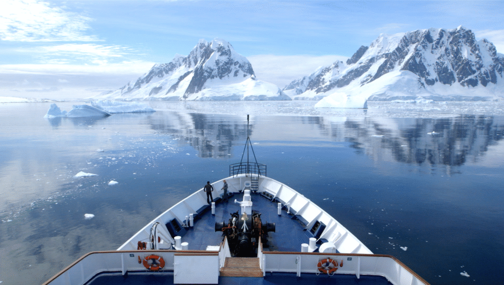 Antarctica cruise: Ship bow with snowy mountains and icebergs in the distance.