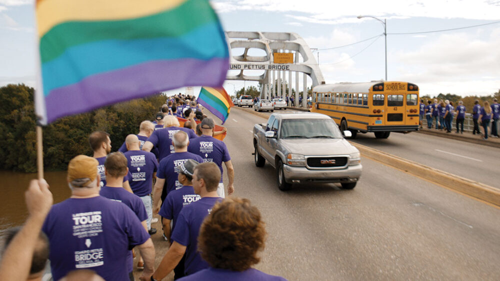 Gay Chorus Deep South marches across Edmund Pettus Bridge with rainbow flag.