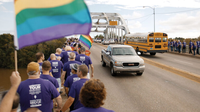 Gay Chorus Deep South marches across Edmund Pettus Bridge with rainbow flag.
