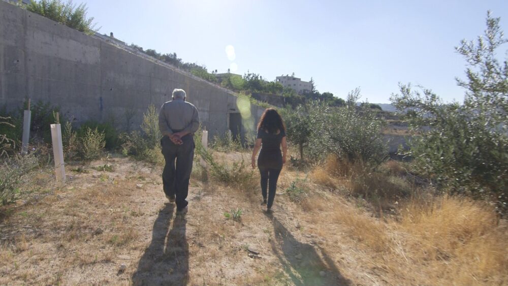 Two people walk along a path near a wall.