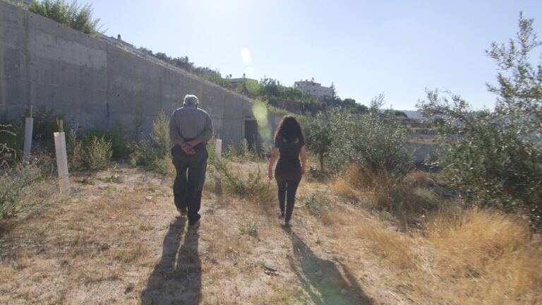 Two people walk along a path near a wall.