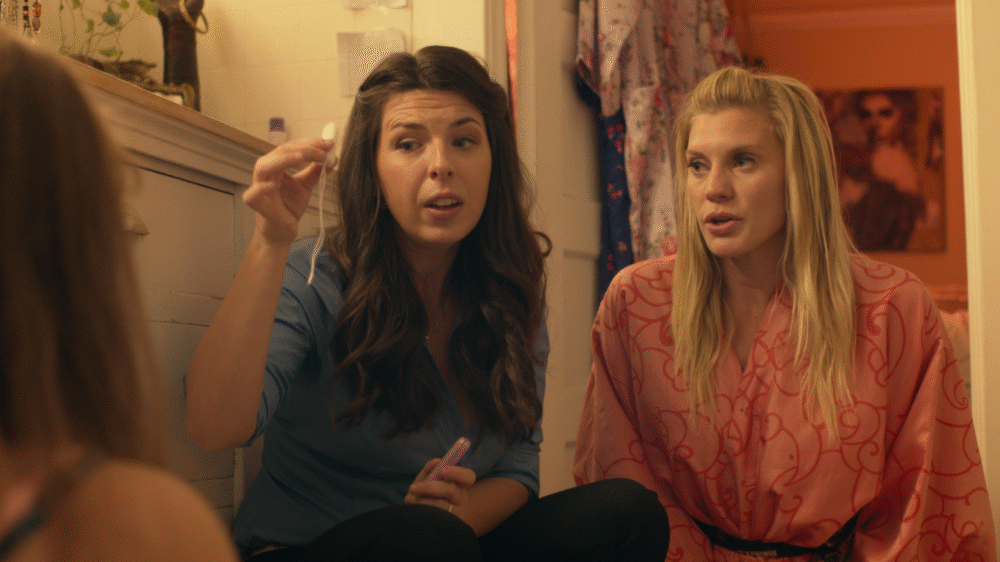 Two women in a bathroom, one holding a tampon.