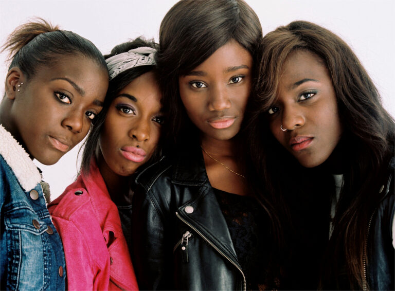 Four young Black women in stylish jackets pose together, embodying themes of "Girlhood"