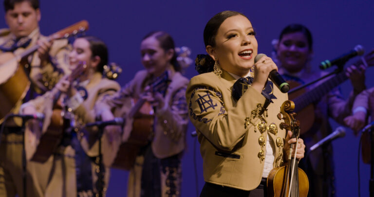 Mariachi singer performing with band in traditional attire.