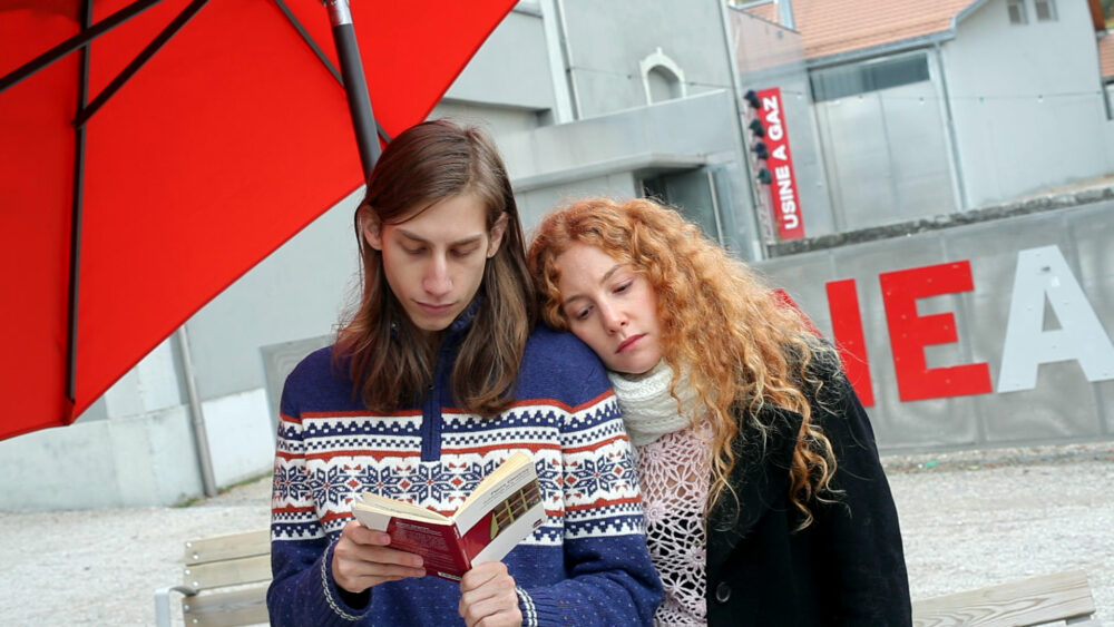 Couple reading under red umbrella; "Usine a Gaz" sign visible.