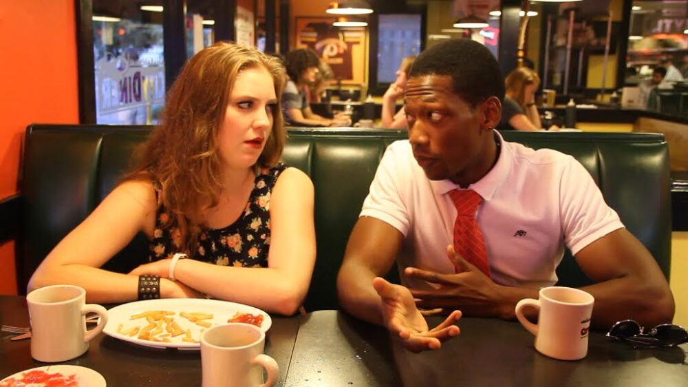 Man and woman in diner booth with fries and coffee, engaged in conversation.