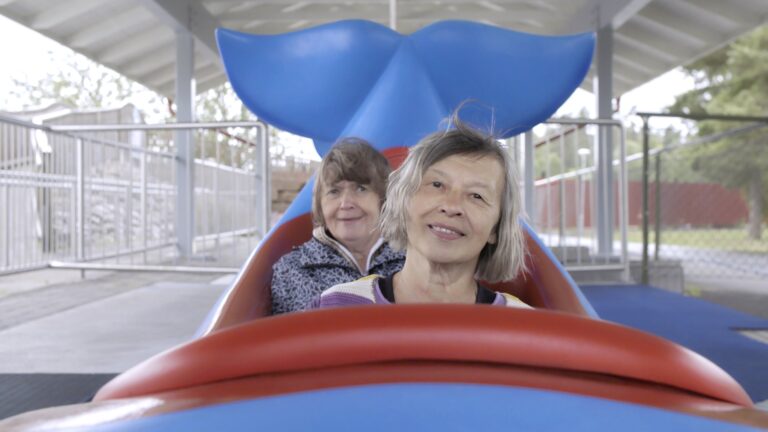 Two women smiling in a blue whale-shaped play structure.