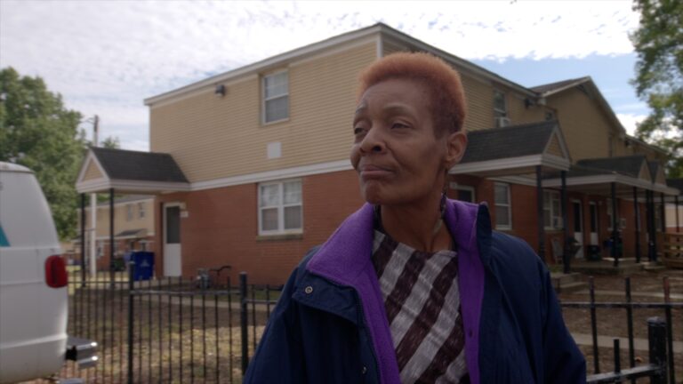 Woman stands in front of brick apartment building.