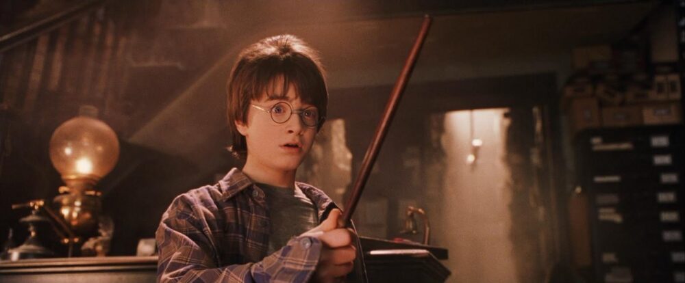 Harry Potter in Harry Potter and the Sorcerer's Stone holds his wand with a surprised expression.