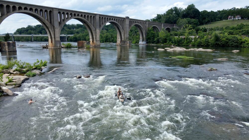 Canoeists paddling in rapids under a large bridge in Richmond, Virginia.