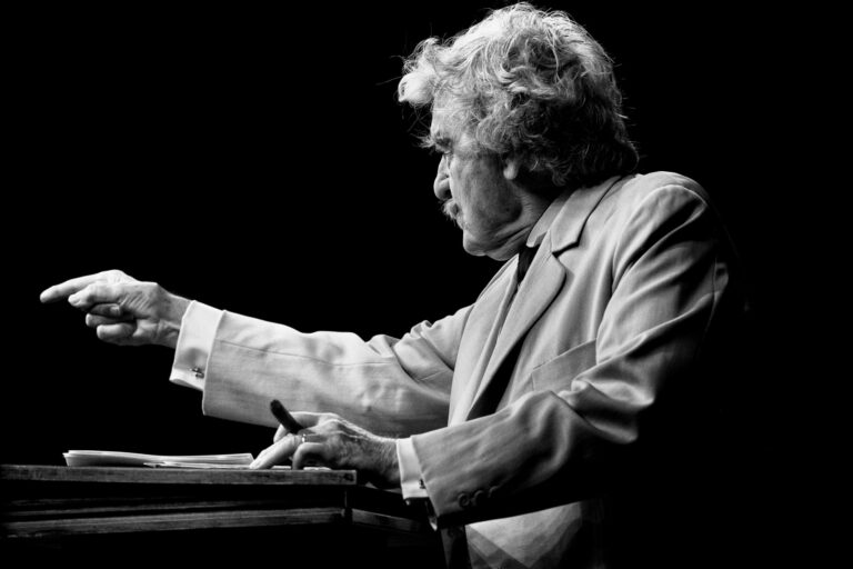 Hal Holbrook as Mark Twain, pointing with a pen in hand.