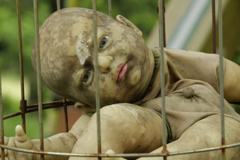 Creepy, weathered baby doll trapped in a rusty cage.