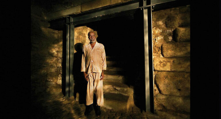 Man in pajamas standing in a stone tunnel entrance.
