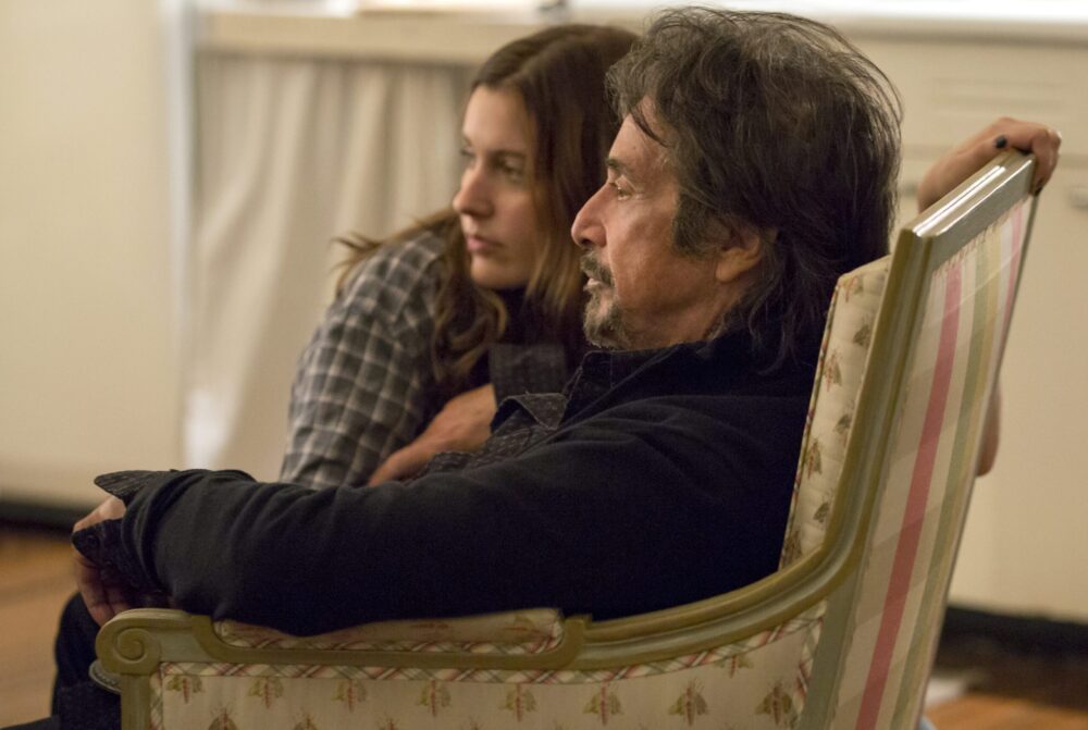Al Pacino in "The Humbling" sits with a younger woman in an armchair, looking thoughtful.