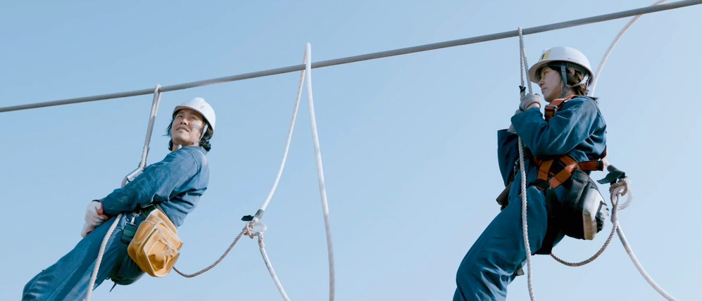 Two workers in blue uniforms on a high-wire safety training course.