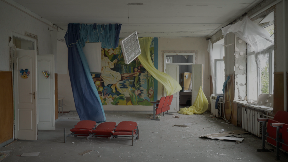 Abandoned room with debris, chairs, and a mural, possibly from "Intercepted