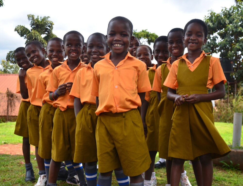 Smiling students in orange shirts and khaki uniforms outside.