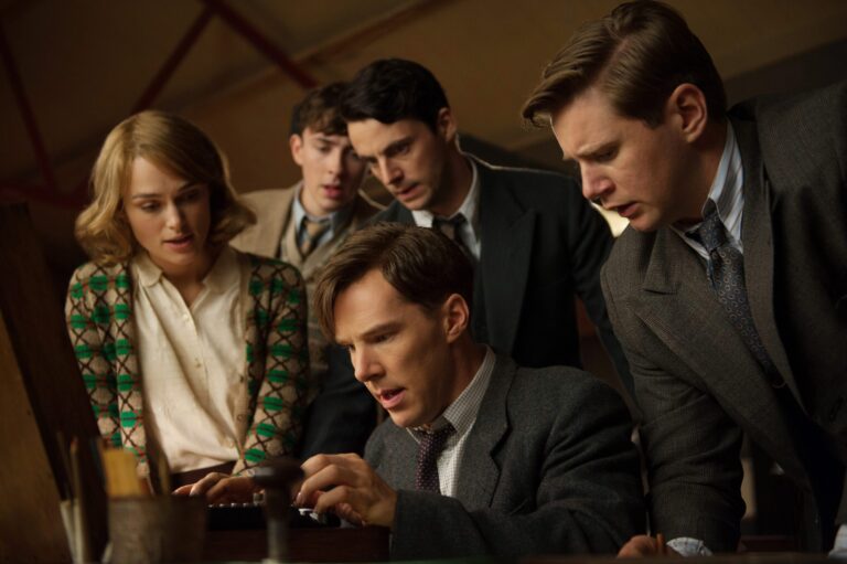 The Imitation Game cast: Benedict Cumberbatch and Keira Knightley working together with a group of men looking over their shoulder.
