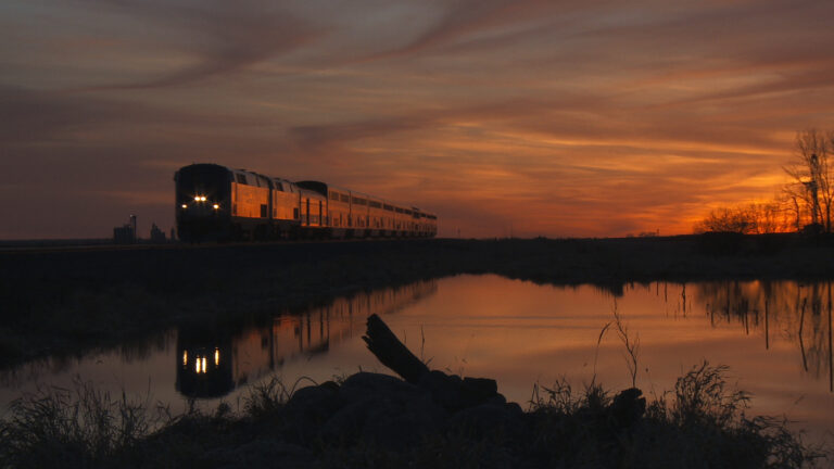 Train at sunset reflected in still water.