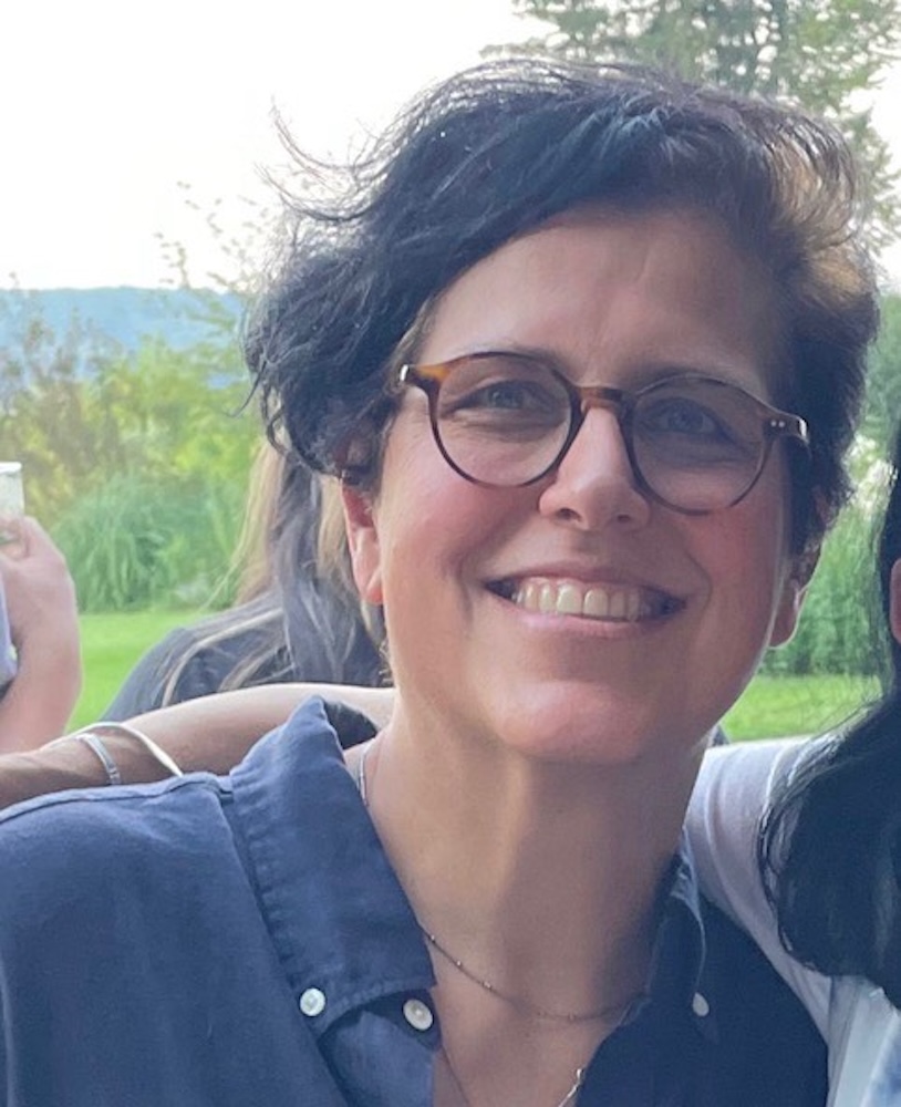 Smiling woman with short dark hair and glasses wearing a blue shirt.