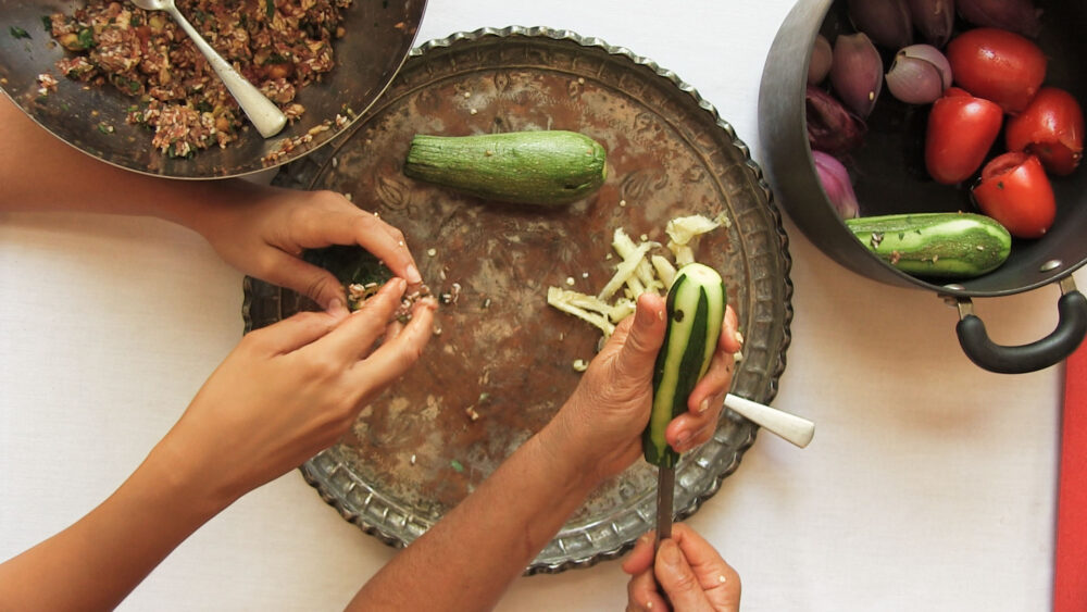 Preparing stuffed zucchini; hands filling zucchini on a copper tray.