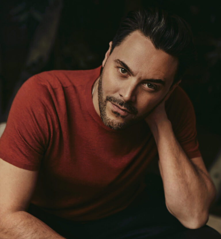 Portrait of actor Jack Huston in a red shirt, looking at the camera.