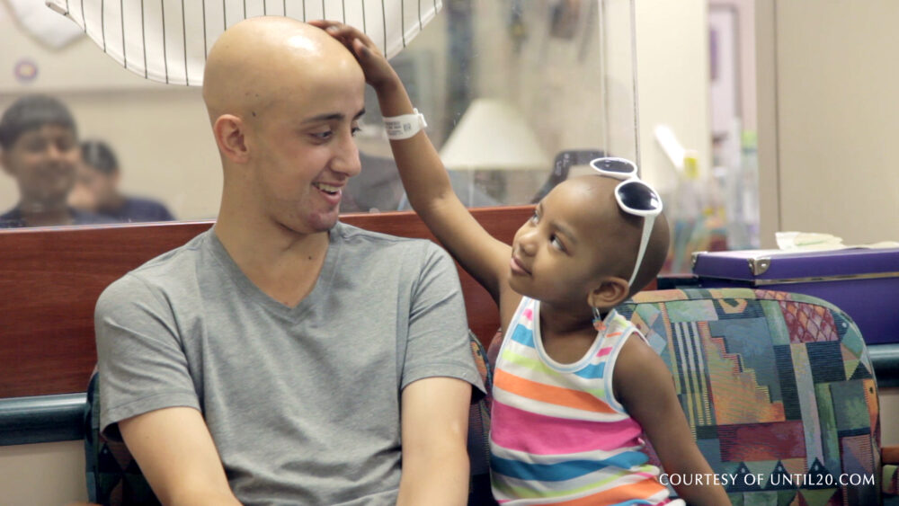 Young boy with cancer touches the head of a man, both smiling.