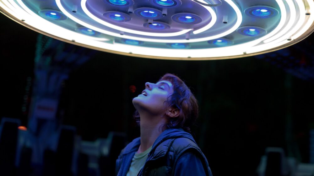 Woman looking up at a futuristic, circular light fixture with blue lights.