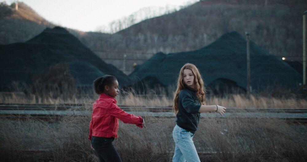Two girls dancing near coal piles and train tracks.