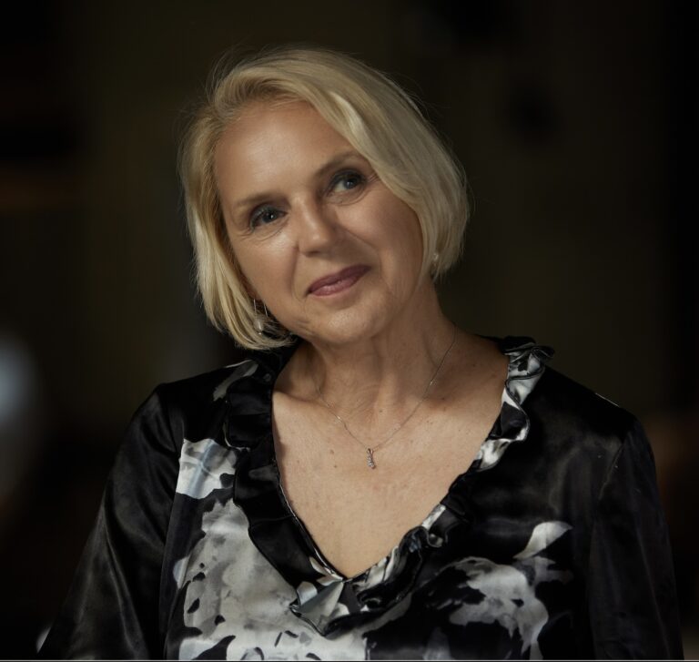 Portrait of Kalina Ivanov, fair-skinned woman with blonde hair, wearing a black and white floral top.