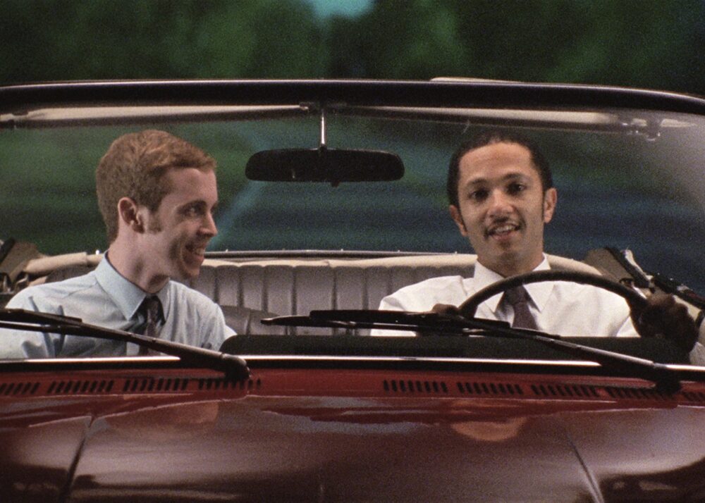 Two men riding in a convertible car.